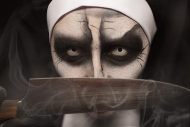 Photo of Scary devilish nun with knife on black background, closeup. Halloween party look