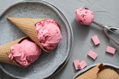 Delicious pink ice cream in wafer cones with candies on grey table, flat lay