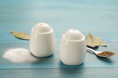 Photo of White ceramic salt and pepper shakers, bay leaves with spoon on turquoise wooden table, closeup