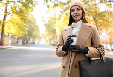 Beautiful young woman with stylish leather gloves and cup of coffee on city street