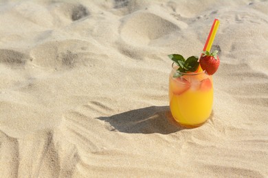 Glass of refreshing drink with strawberry on sandy beach, space for text