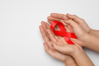 Woman and girl holding red ribbon on white background, top view with space for text. AIDS disease awareness
