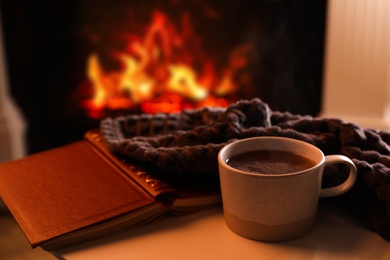Photo of Cup of hot drink and book on table near fireplace indoors