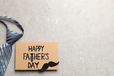 Photo of Card with phrase Happy Father's Day, paper mustache and necktie on light grey background, flat lay. Space for text
