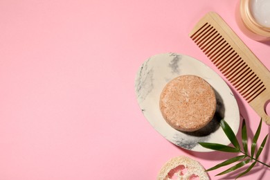 Flat lay composition of solid shampoo bar, leaf and comb on pink background. Space for text