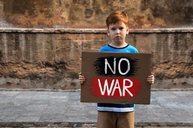 Sad boy holding poster with words No War outdoors. Space for text