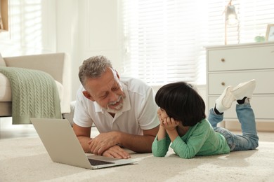 Grandfather and his grandson using laptop together on floor at home