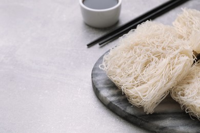 Photo of Uncooked rice noodles, soy sauce and chopsticks on light grey table. Space for text