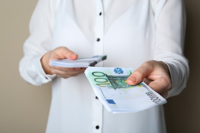 Woman holding 100 Euro banknotes on beige background, closeup. Money exchange