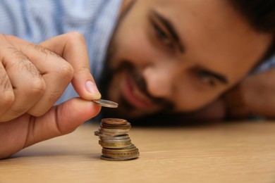 Man stacking coins at wooden table, focus on hand. Money savings