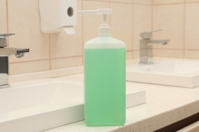 Photo of Dispenser bottle with green antiseptic gel in public bathroom