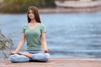 Teenage girl meditating near river. Space for text