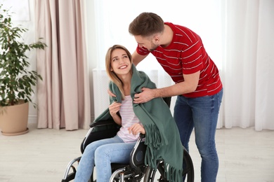 Man covering woman in wheelchair with plaid at home. Helping disabled