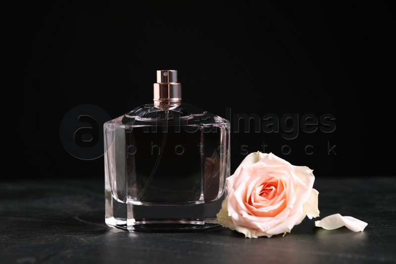 Bottle of perfume and beautiful rose on black table