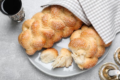 Photo of Homemade braided bread with sesame seeds and goblet on grey table, flat lay. Traditional Shabbat challah