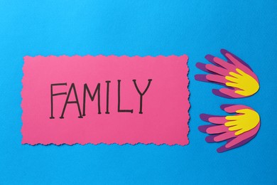 Photo of Card with text Family and paper palms on light blue background, flat lay