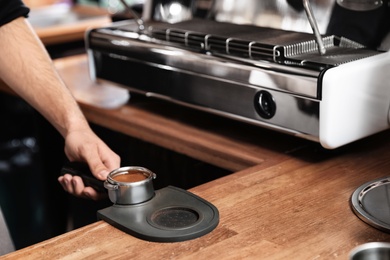 Barista holding portafilter with milled coffee on tamp mat at bar counter, closeup. Space for text