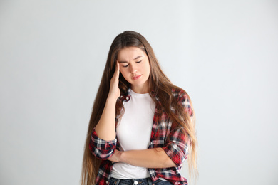 Young woman suffering from headache on light background