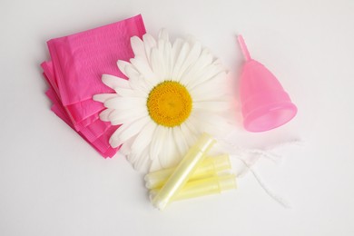 Tampons, pads, menstrual cup and chamomile flower on white background, top view