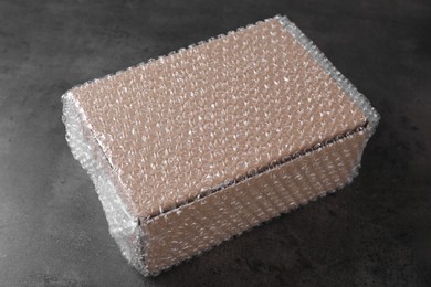 Photo of Cardboard box covered with bubble wrap on dark grey table