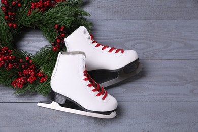 Pair of ice skates and Christmas wreath on grey wooden background, flat lay