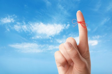 Woman showing index finger with tied red bow as reminder against blue sky, closeup