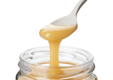 Honey dripping from spoon into jar on white background
