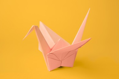 Photo of Origami art. Beautiful pale pink paper crane on orange background