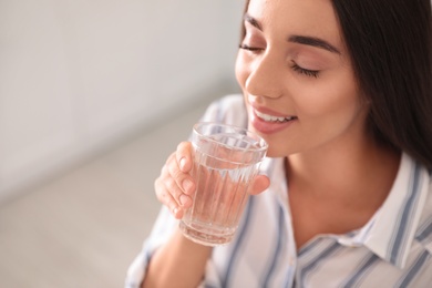 Young woman drinking pure water from glass indoors, closeup. Space for text
