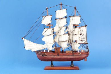 Miniature model of old ship with white sails on blue background