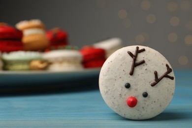 Tasty reindeer Christmas macaron on light blue table against blurred festive lights, space for text