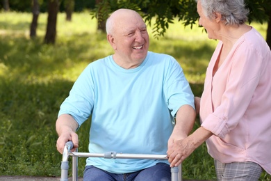 Elderly woman helping her husband with walking frame outdoors