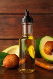 Photo of Glass bottle of cooking oil and fresh avocados on wooden table