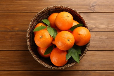 Delicious ripe oranges in wicker bowl on wooden table, top view