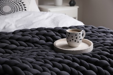 Tray with cup of coffee and soft chunky knit blanket on bed indoors