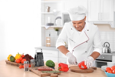 Photo of Professional chef cutting pepper on table in kitchen