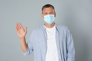 Man in protective mask showing hello gesture on grey background. Keeping social distance during coronavirus pandemic