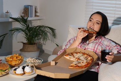 Overweight woman eating pizza with cola on sofa at home