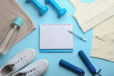 Flat lay composition with sportswear, notebook and dumbbells on light blue background, space for text. Gym workout plan