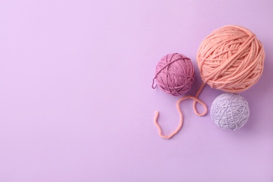 Soft colorful woolen yarns on lilac background, flat lay. Space for text
