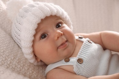Cute little baby wearing white warm hat on knitted blanket, closeup