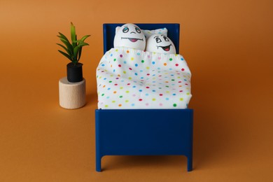 Eggs with drawn happy faces in small bed on orange background