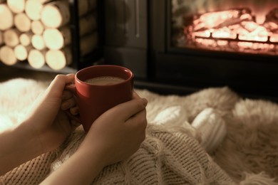Woman with hot drink resting near fireplace at home, closeup