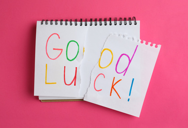 Torn phrase GOOD LUCK written in notebook on pink background, top view