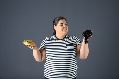 Photo of Overweight woman with grapes and hamburger on gray background