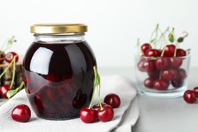 Jar of pickled cherries and fresh fruits on light table, closeup