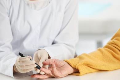 Doctor taking patient's blood sample with lancet pen in hospital, closeup. Diabetes control