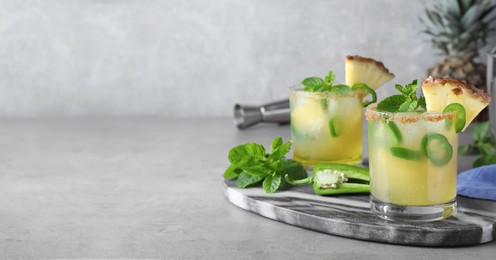 Glasses of spicy pineapple cocktail with jalapeno and mint on grey table. Space for text