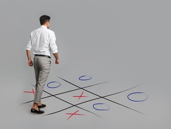 Man and illustration of tic-tac-toe game on grey background, back view. Business strategy concept 