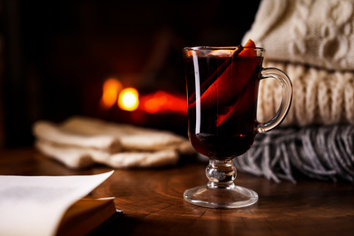 Tasty mulled wine, book, knitwear and blurred fireplace on background